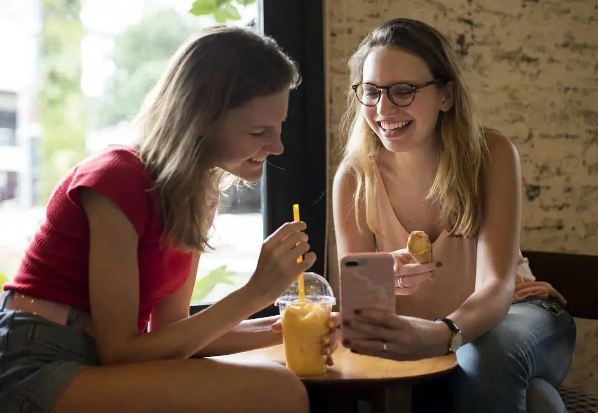 Two students enjoying snack while looking at phone